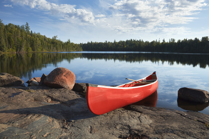 Red canoe on rocky shore of calm lake with pine trees